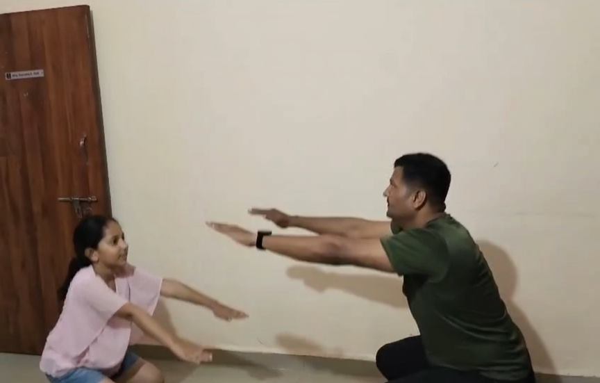 A participant practicing a stretch at home with his daughter
